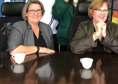 Two woman sit at a boardroom table, smiling. Text says, A Story of thankfulness. Drs. Kathryn Johnson and Amy Hebert.