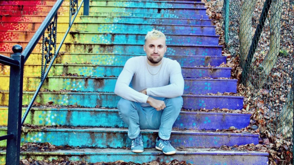 A man with spiky blonde hair and casual clothes sits on a set of steps that are painted in green, blue and purple. The headline is California has got me dreaming. As an autic solo traveler, I have been to many of our earth's most breathtaking sites. However. . . Orange text invites us to Read More.