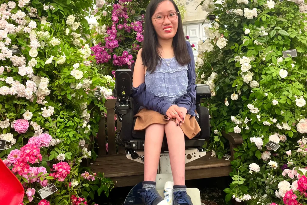 A woman poses among white and pink rose bushes.Text reads, An accessible visit to London's British Museum by Alicia Loh @ExploreDisabled. Read More.