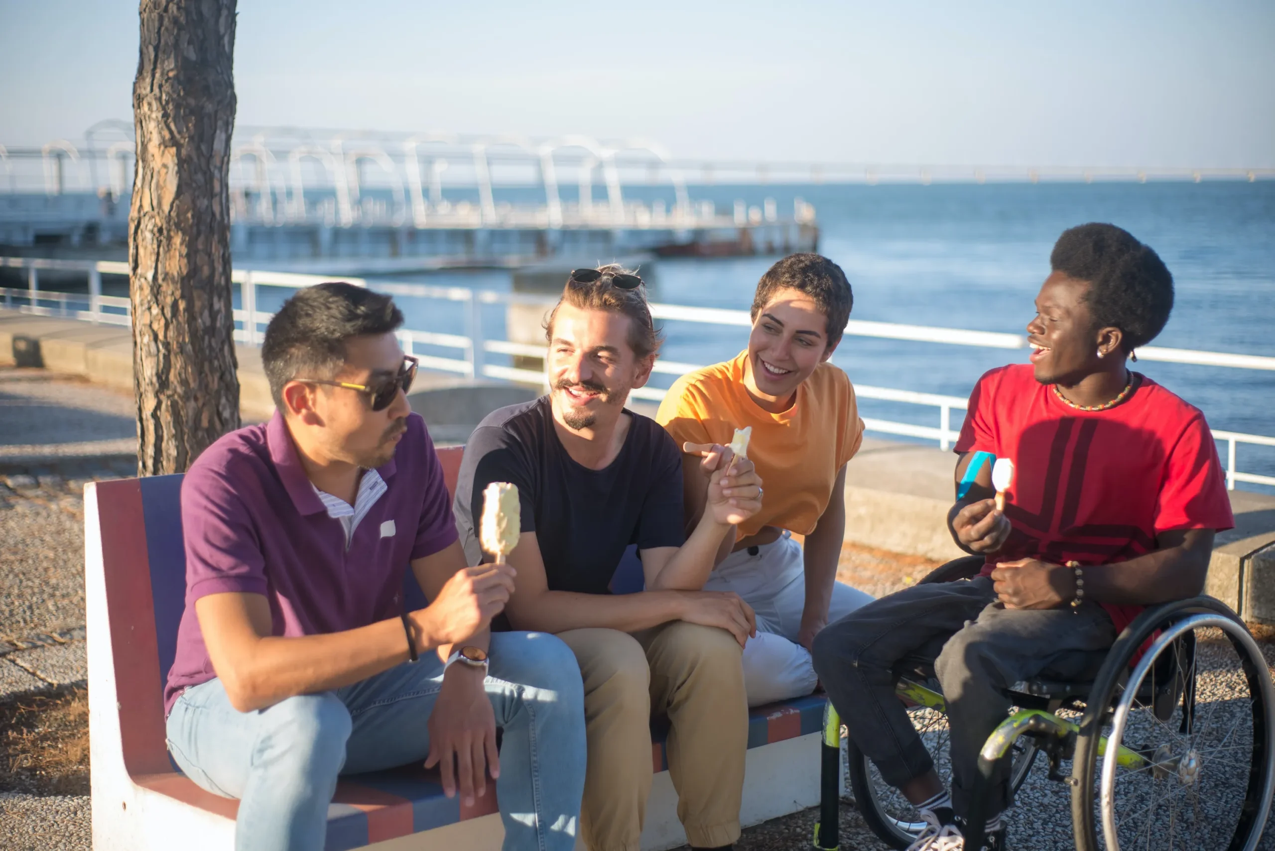 Four people sit outside on a seawall eating popsicles, the water in the distance.