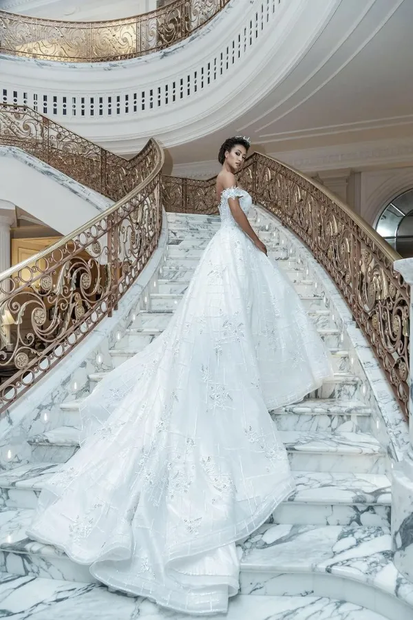 A woman standing in the center of a luxurious hall, wearing a long, dramatic, high-collared emerald green gown with puffed sleeves. The hall features a polished black and white marble floor, tall columns, and large arched windows reflecting the ornate interior and chandeliers.