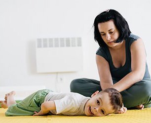 A child lays smiling on the floor while a woman with a focused expression leans toward him.