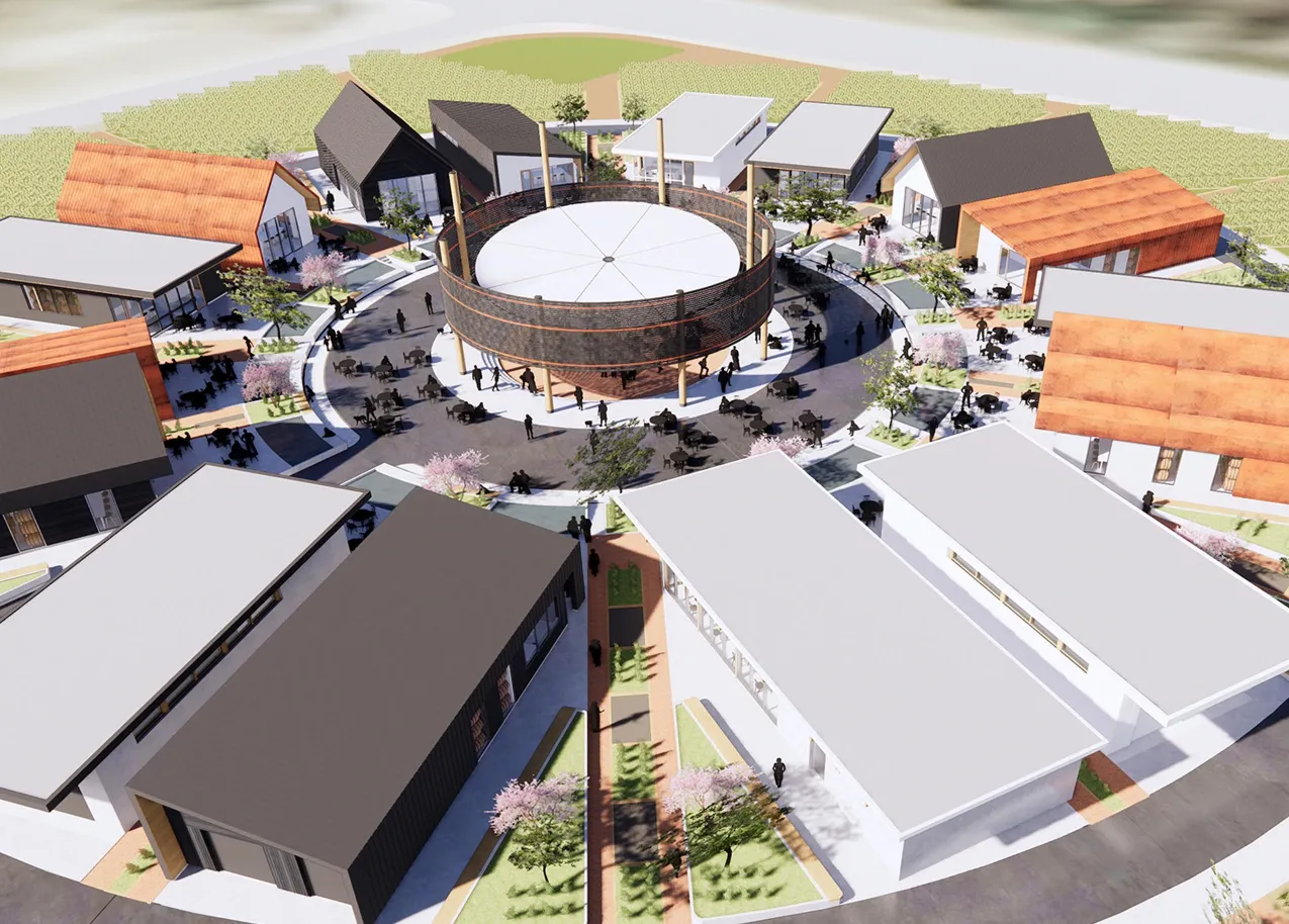 A high-angle, architectural rendering of a modern mixed-use development, likely a "village" concept, featuring a circular central building resembling a covered silo or wine vat, surrounded by a ring of modern farmhouse-style buildings with varied rooflines (black, white, and terracotta). The central plaza area is filled with small figures, tables, and trees, suggesting an outdoor gathering space. The buildings are set within a landscaped area, possibly adjacent to vineyards or a field.