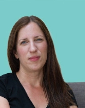 A headshot of a woman with long brown hair and light eyes, wearing a black top. She is looking directly at the camera with a neutral expression, against a solid turquoise background.