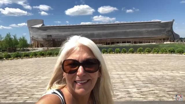 A silver-haired woman wearing sunglasses smiles under a blue sky studded with puffy clouds.