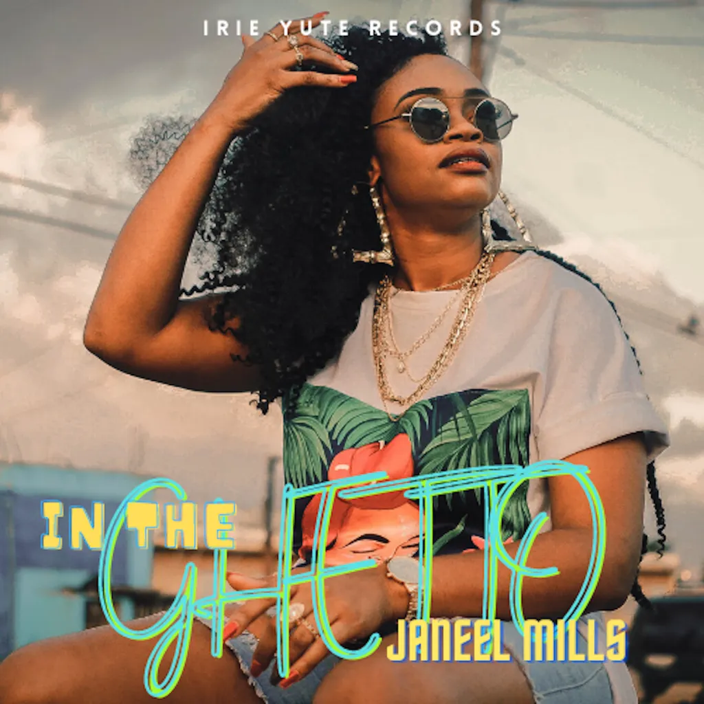 Cover art for the song "In The Ghetto" by Janeel Mills, released by Irie Yute Records. The photo features the artist, a young Black woman with long, dark, curly hair, posing outdoors on a sunny day. She is wearing round sunglasses, large hoop earrings with letter charms, and multiple gold necklaces and rings. She has one hand running through her hair and is wearing a white t-shirt with a green and red tropical print. Large, colorful, outlined text overlays the image, reading "IN THE GHETTO," with the artist's name, "JANEEL MILLS," below it. The record label "IRIE YUTE RECORDS" is written across the top.
