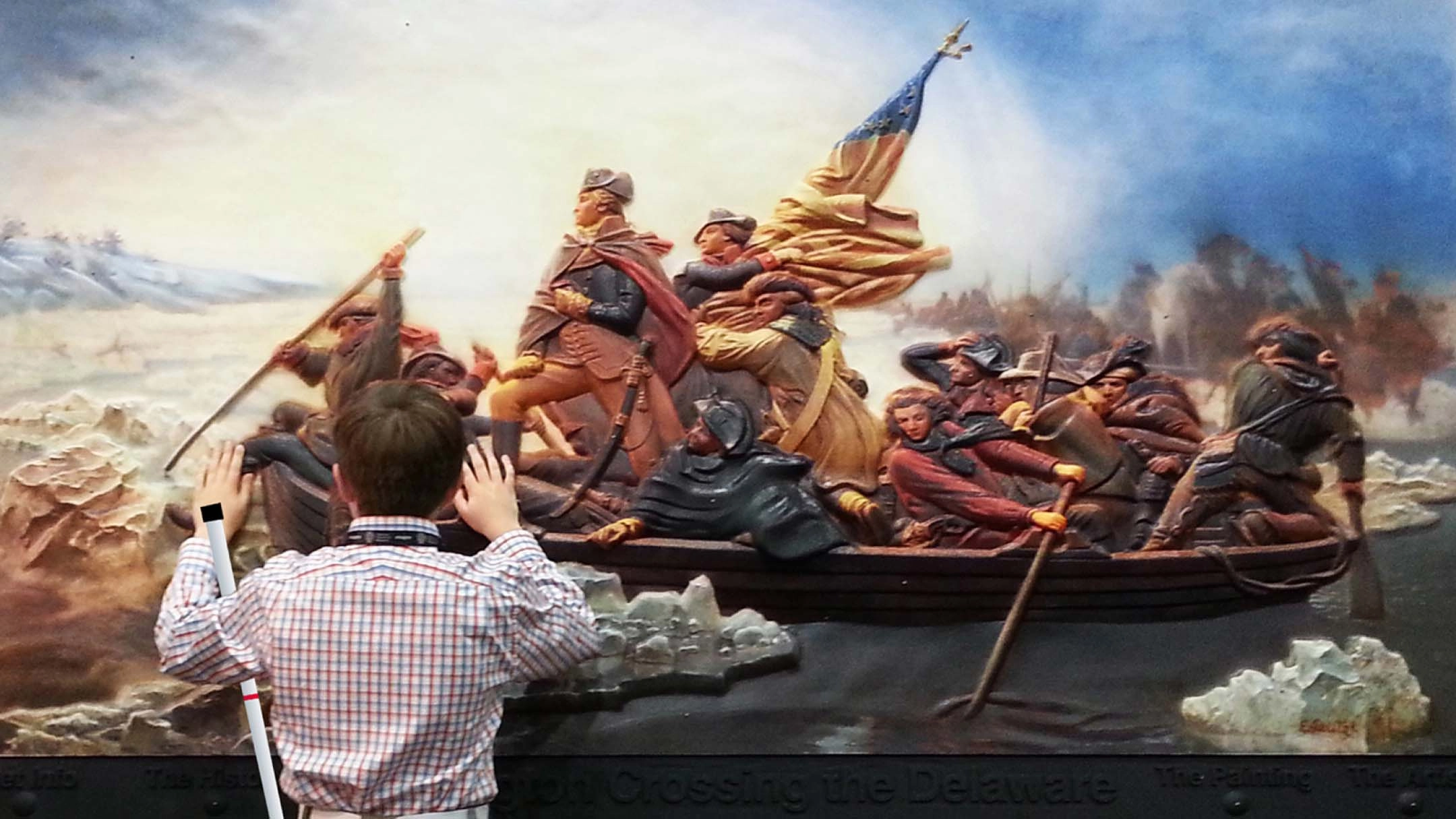 A young boy, viewed from the back, reaches up with both hands to feel a large, three-dimensional tactile relief of the famous painting, "Washington Crossing the Delaware." He is wearing a plaid shirt and holding a white cane in his left hand. The tactile artwork depicts George Washington and soldiers in a boat moving through icy water, set against a dramatic sky.