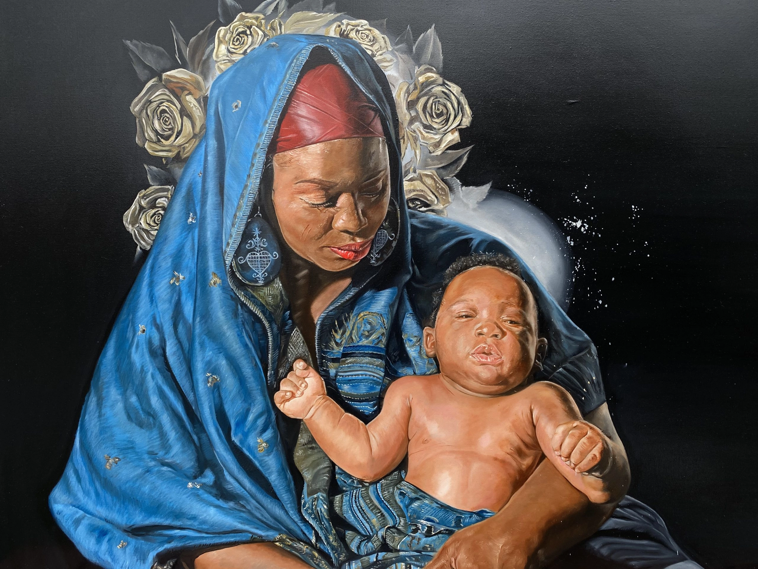 A striking oil painting of a Black woman, draped in a deep blue, textured garment and wearing a red headscarf, holding an infant against a dark background. White and pale yellow roses form a halo-like wreath around the woman's head. The infant is shirtless and looks directly at the viewer.