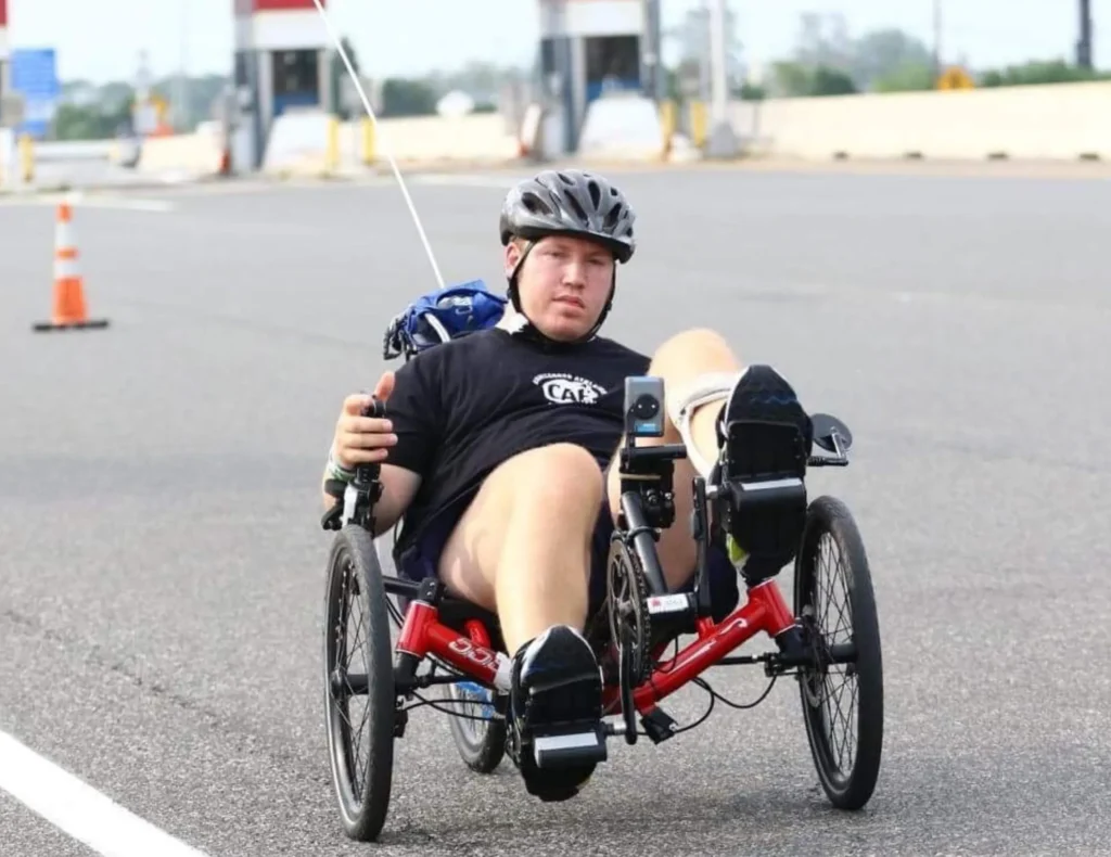 On an outdoor asphalt track, a man pedals an adapted red bicycle.