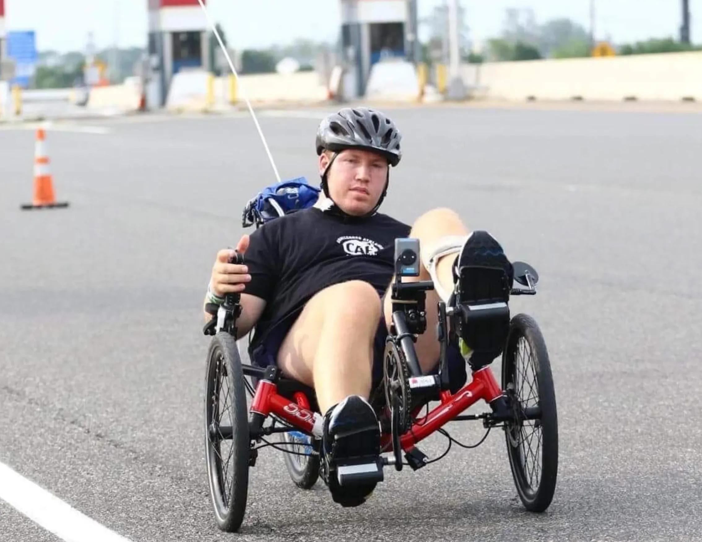On an outdoor asphalt track, a man pedals an adapted red bicycle.