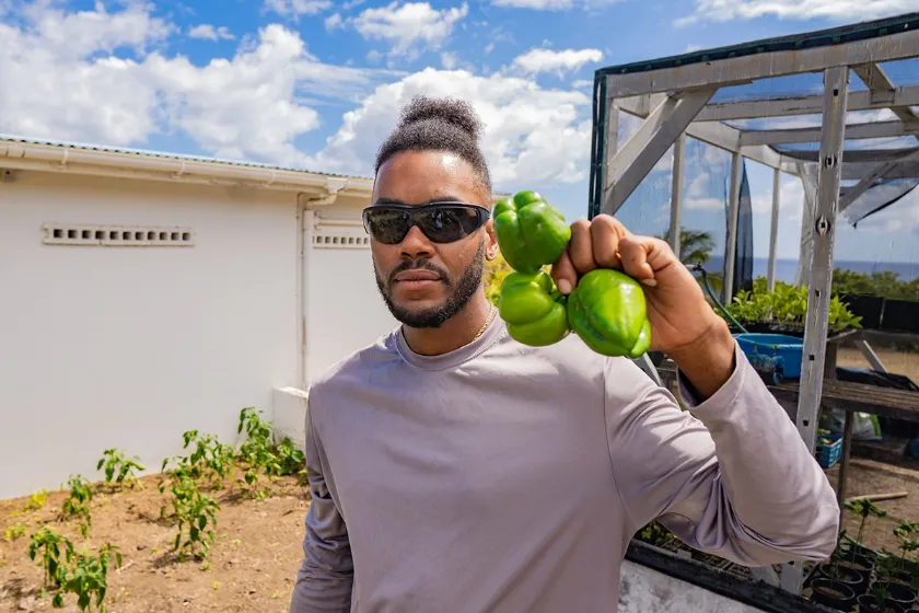 A man with his hair pulled back, wearing a bright red dress shirt and a black tie, sits in a recording studio. He looks to the side with his hands clasped in front of him. In the background are sound-dampening panels and two large monitors, one displaying a logo and the text "TWICH STUDIO."