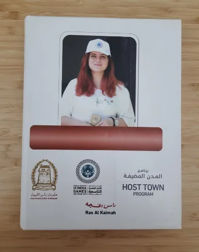 Cover of the Ras Al Khaimah Host Town Program booklet for the IX MENA Special Olympics Games 2018, showing a photo of a female volunteer wearing a white cap and shirt.