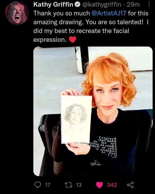 A screenshot of a tweet from Kathy Griffin thanking the artist, @ArtistAJ17. Kathy Griffin, a woman with orange-red hair and a black shirt, is holding up a small, realistic pencil drawing of herself and recreating the drawing's facial expression.
