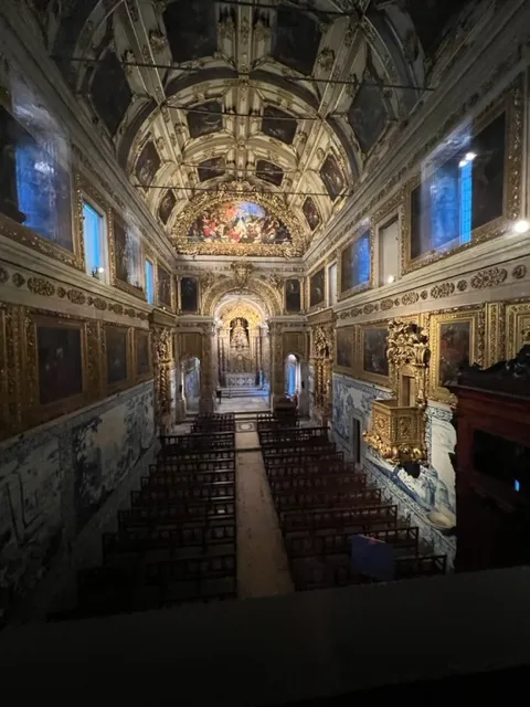 Interior of an ornate, historic chapel or church with a vaulted ceiling, elaborate gold detailing, and blue and white azulejo tiles lining the walls.