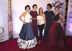 The image shows five women posing together on a red carpet in front of a backdrop that includes the word "LEOs" and logos of various sponsors. They are dressed in formal evening wear, featuring gowns with different styles and colors. The backdrop suggests that this event is an awards ceremony or a similar formal occasion. The women appear to be attendees or honorees at the event, likely linked to the film or entertainment industry given the context of an awards ceremony. It is actually the Leo Awards 2015.Chloe is one of the ladies.