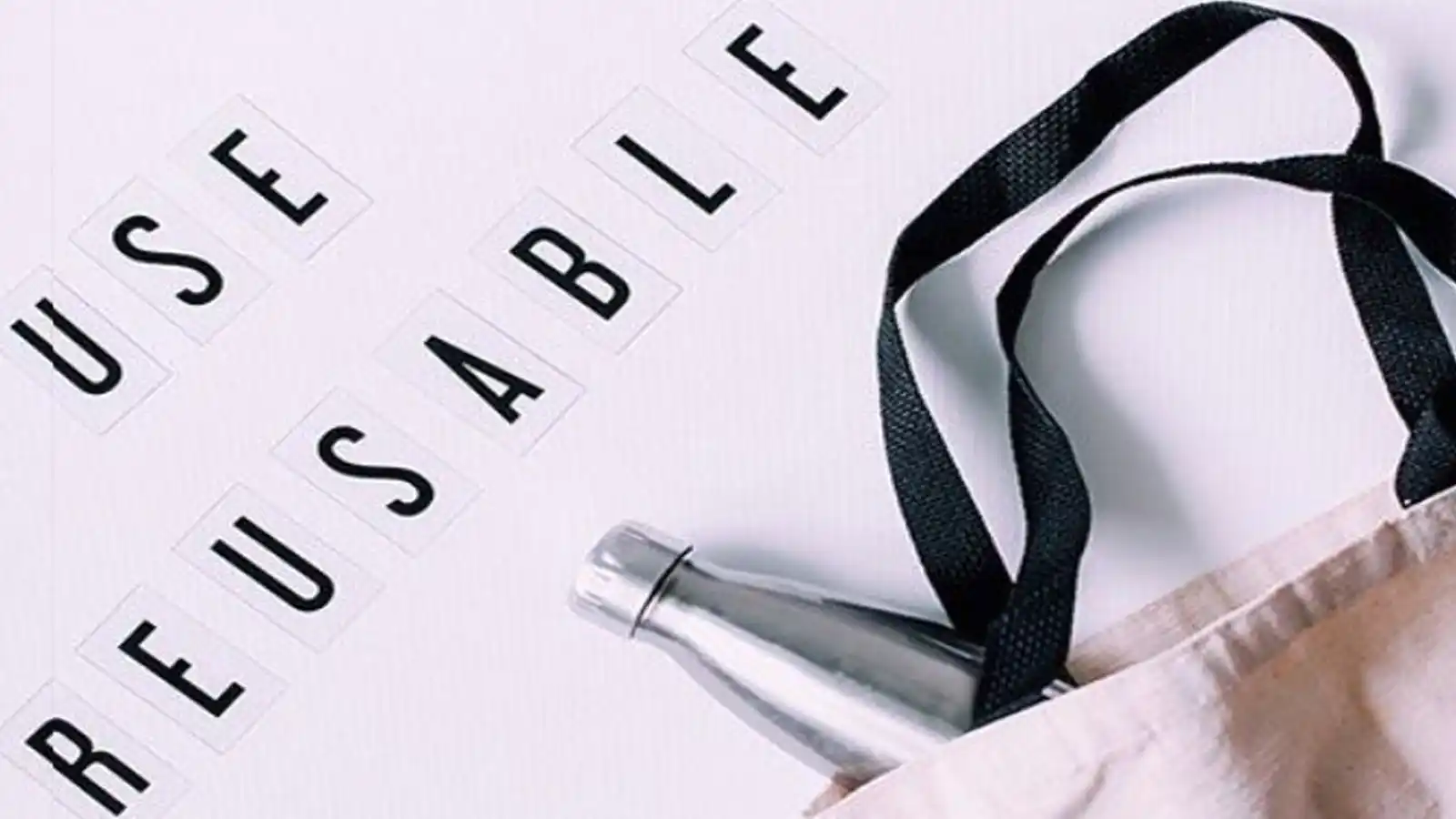 The image shows a reusable stainless steel water bottle partially tucked into a beige fabric bag with black straps. The words "USE REUSABLE" are displayed to the left of the bag, spelled out in black capital letters on individual square tiles arranged in a vertical and horizontal format. The image promotes sustainability and encourages the use of reusable items to reduce waste.
