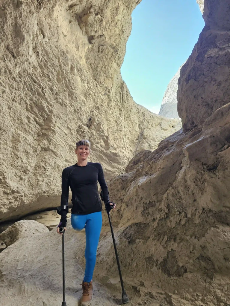 A woman standing in a rocky canyon with crutches, wearing athletic attire, and surrounded by towering natural formations.