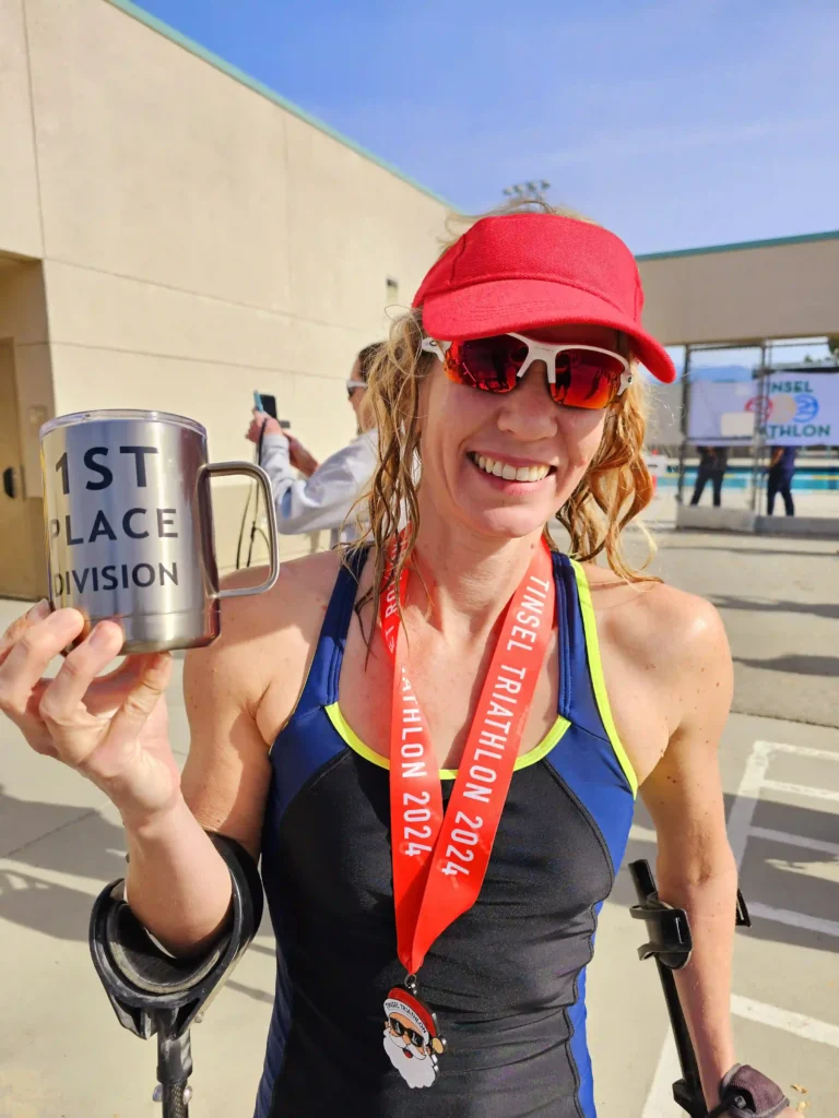 A triumphant moment at a triathlon event, showing a woman holding a "1st Place" mug and medal, wearing sportswear and sunglasses.