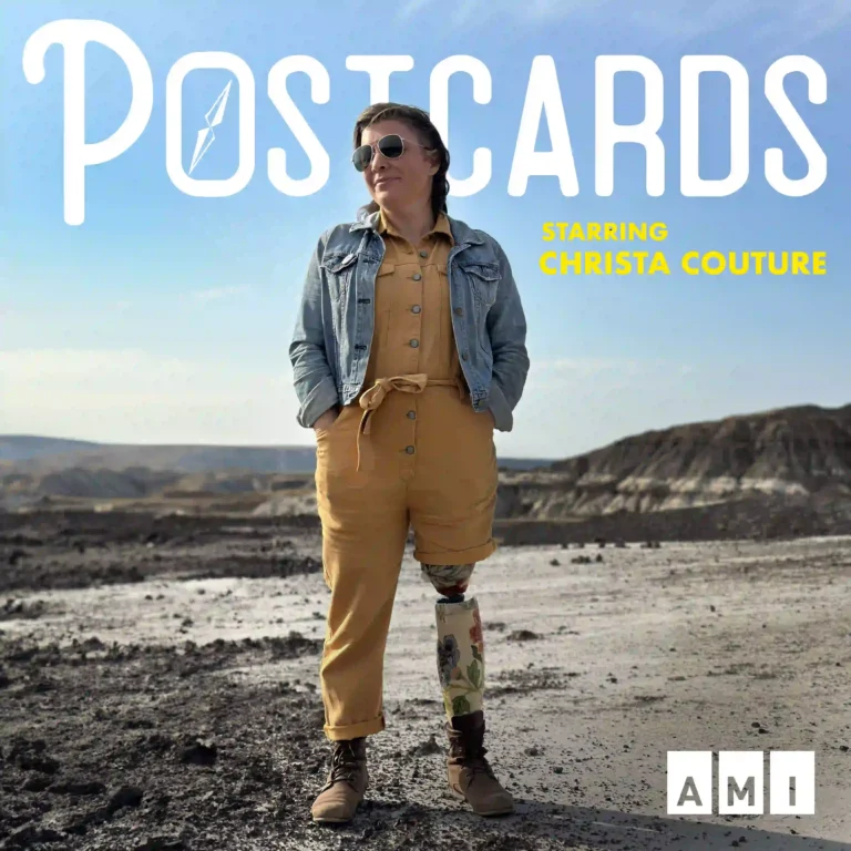 A vibrant poster for the series 'Postcards,' starring Christa Couture. Christa stands confidently in a rugged, rocky landscape under a bright blue sky. She’s wearing a mustard-yellow jumpsuit, a denim jacket, and sunglasses, exuding style and strength. Her floral-patterned prosthetic leg is prominently featured, adding a unique and beautiful touch. The title 'Postcards' is written in bold white letters at the top, with a paper airplane symbol nestled in the text, and 'starring Christa Couture' in yellow. The AMI logo sits in the bottom-right corner.