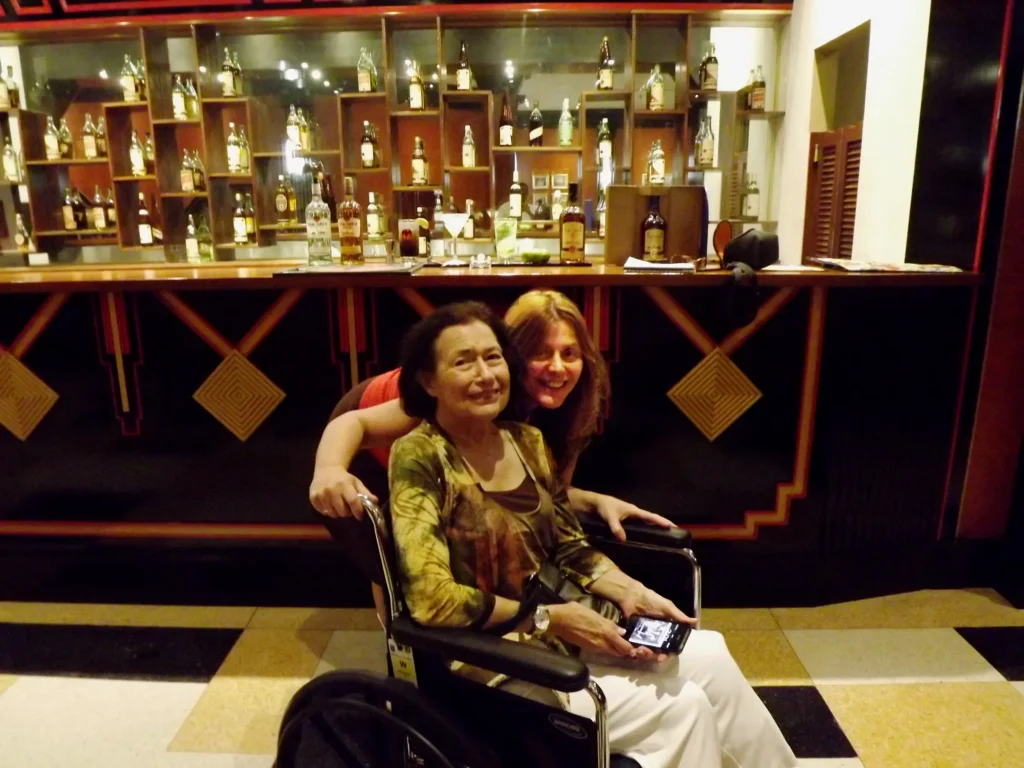 A woman in a wheelchair holds a smartphone, with a vibrant bar display of bottles behind her, suggesting a social atmosphere.