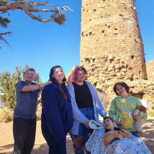 A group of five people poses in front of a historic stone tower, surrounded by desert landscape and clear blue skies.