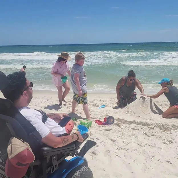 A group of people enjoying a sunny day at the beach, playing in the sand with buckets and creating sand sculptures by the ocean.