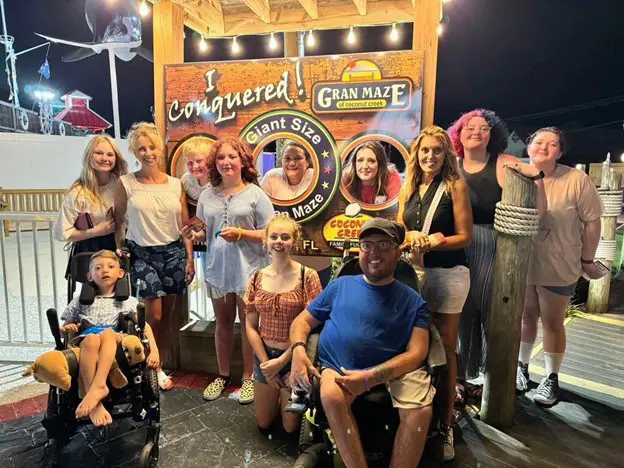 A group of people celebrates in front of a colorful backdrop, holding a sign that reads "I Conquered! Gran Maze." It’s a festive atmosphere at night.