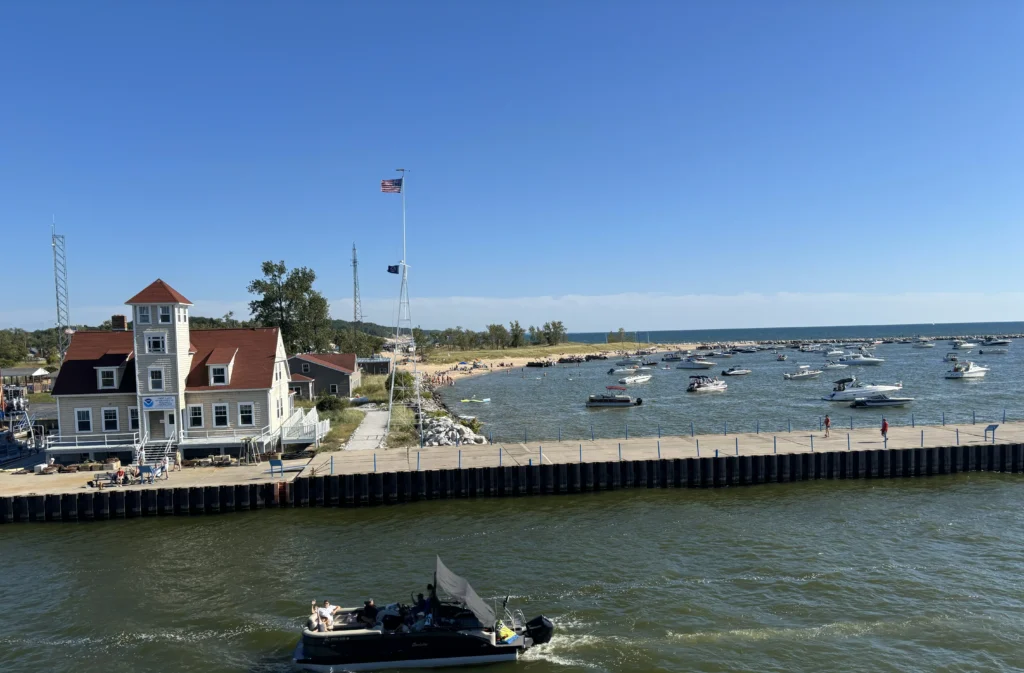 A scenic view of a marina with boats, a sandy beach, and a historic building, framed by clear blue skies.