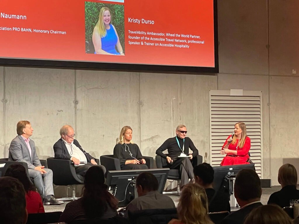 A panel discussion featuring four speakers, with a PowerPoint presentation displaying participants' names and titles in a conference setting.