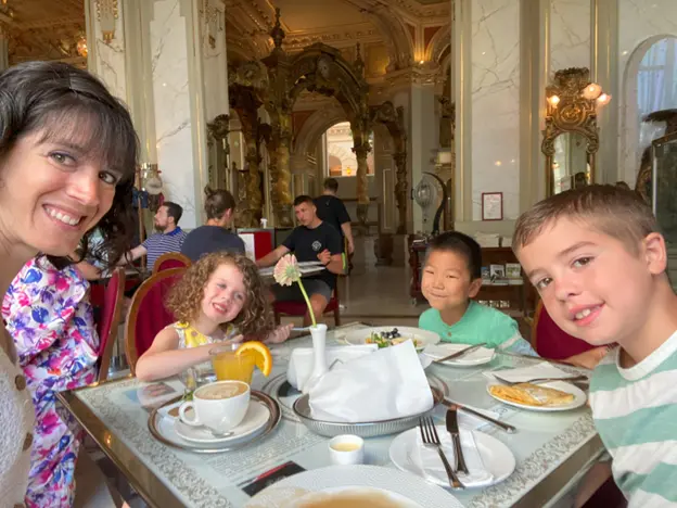 A luxurious restaurant scene featuring a table with children enjoying breakfast, surrounded by elegant decor and other diners in the background.