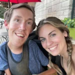 A man and woman in wheelchairs smiling warmly at the camera, showcasing joy and inclusivity.