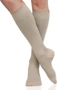 A pair of beige knee-high socks displayed, with smooth ribbed texture and slight sheen, crossed at the ankles.