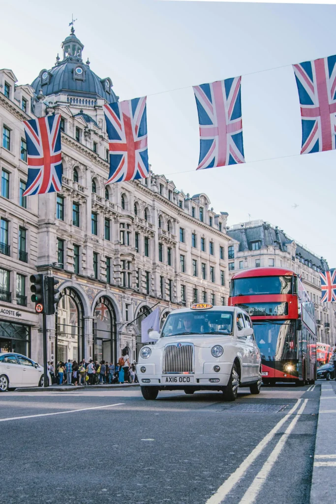A large building adorned with numerous flags, set against a clear sky, with a road in front and vehicles, including buses and cars, nearby.