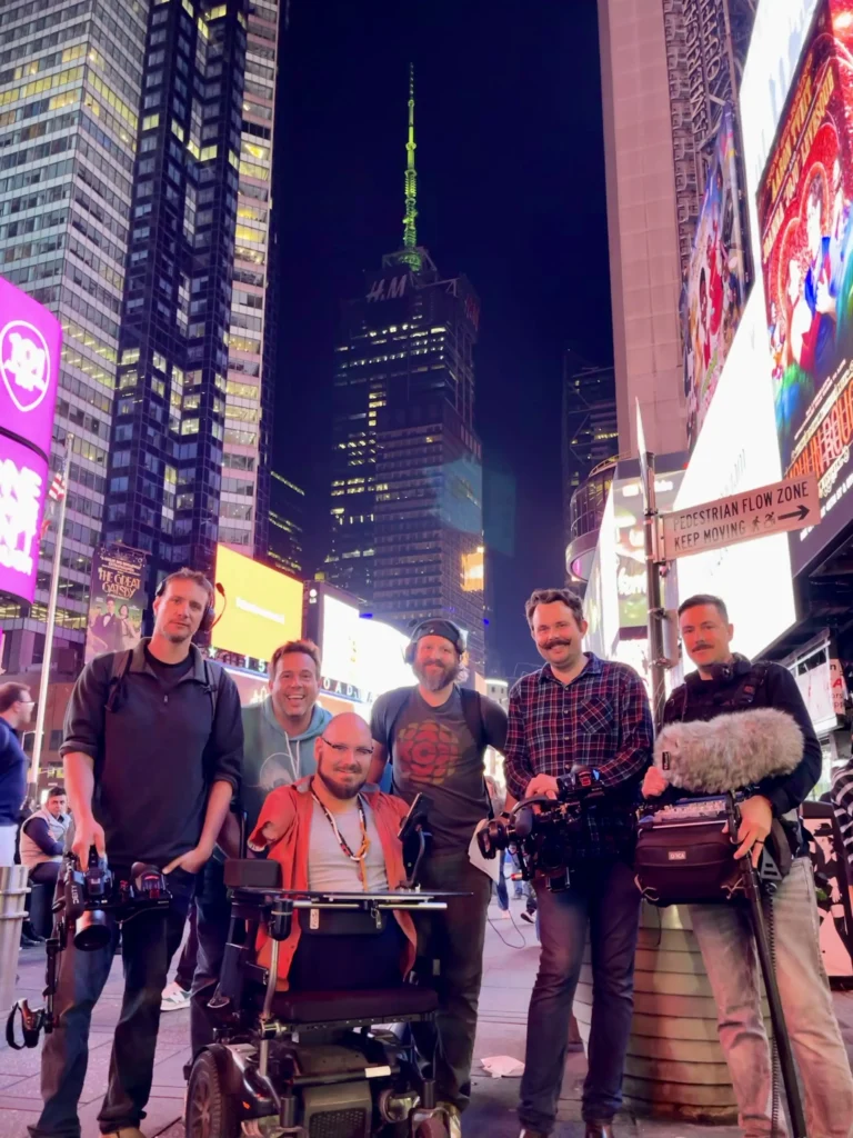 A group of filmmakers poses in Times Square at night, surrounded by bright neon lights and towering skyscrapers.