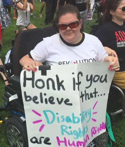 A person in a wheelchair holds a sign reading "Honk if you believe that... Disability Rights are Human Rights" at a rally.