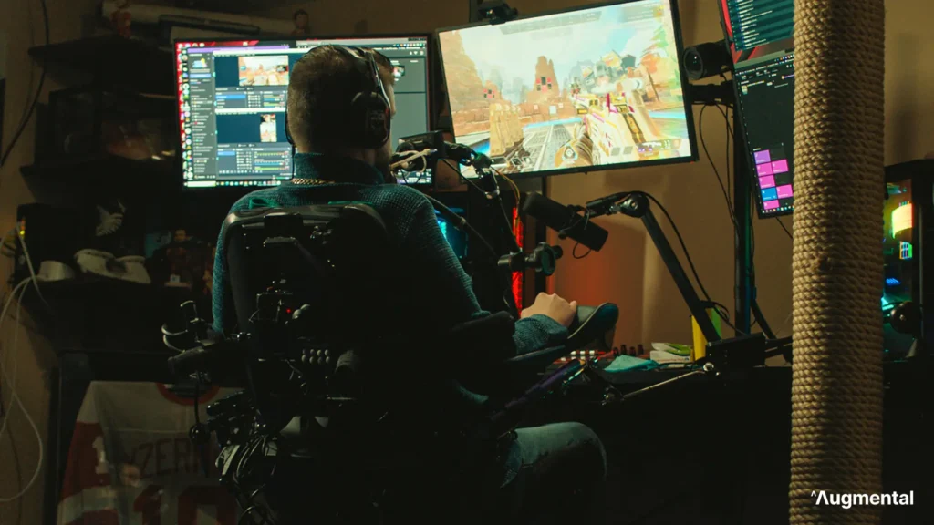 A person in a wheelchair sits at a gaming desk, focused on two monitors displaying gameplay and streaming software.