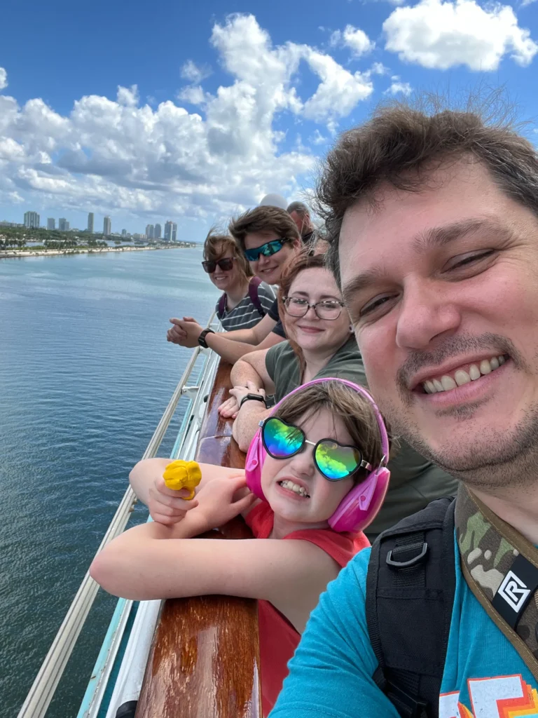 A group of people standing on a ship's railing, enjoying a view of the water and city skyline under a partly cloudy sky.