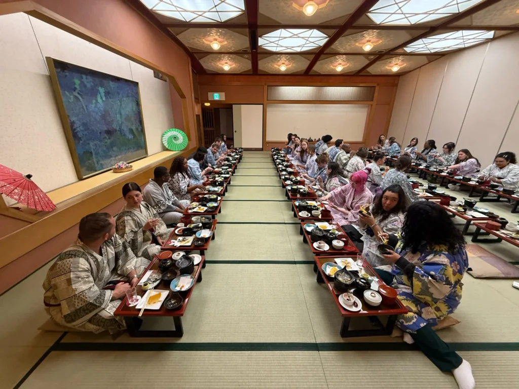 Large group seated at long tables in a Japanese-style dining room, enjoying a meal.