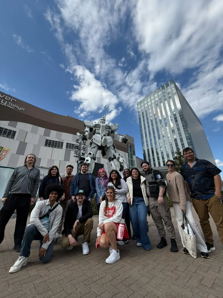 Group of people posing in front of a large robot statue at a modern building in Tokyo.