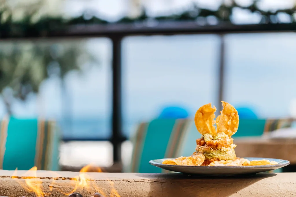 Gourmet seafood appetizer with crispy wonton chips served at an outdoor beachfront restaurant with ocean view in the background.