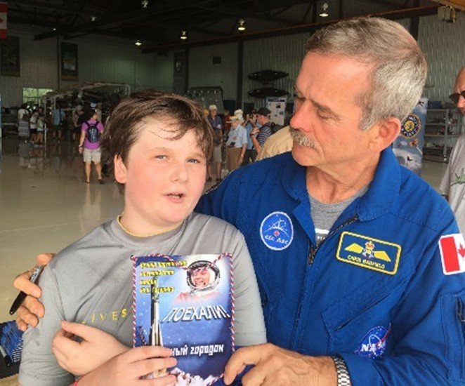 Canadian astronaut Chris Hadfield with a young fan holding a space-themed book, taken inside an aircraft hangar during a public event