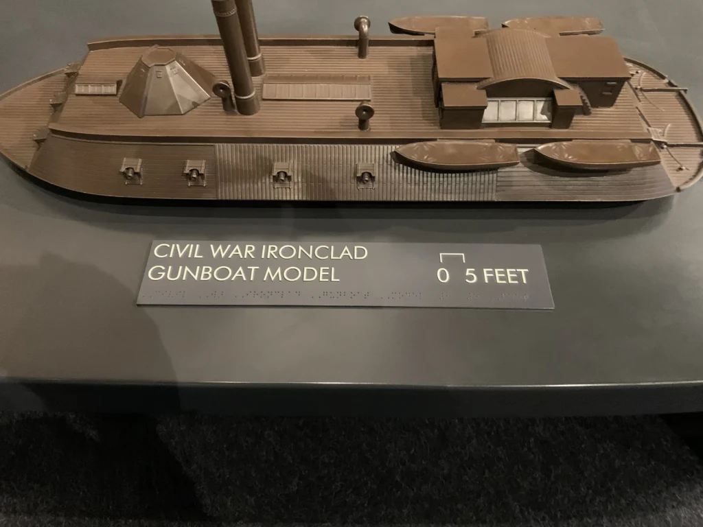 Model of a Civil War ironclad gunboat displayed on a table, with a plaque indicating its scale in feet.