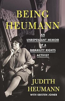 A book cover for "Being Heumann: An Unrepentant Memoir of a Disability Rights Activist." The cover has a simple, minimalist design. A black and white photo of the author, a woman with a serious expression and short, dark hair, is in the center. She is looking to the side. The title is in a thin, sans-serif font above and below the photo. The background is a solid, medium-blue color. The author's name, "Judith Heumann," is below the title.