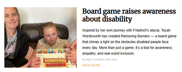 Two people are sitting on a couch, holding a board game box between them. The box's title is "Removing Barriers." Both people are looking at the camera and smiling. The person on the right is in the foreground and has a more direct view of their face.
