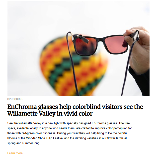 A person's hand holds a pair of red-tinted sunglasses in the foreground. A colorful, out-of-focus hot air balloon is visible in the background.