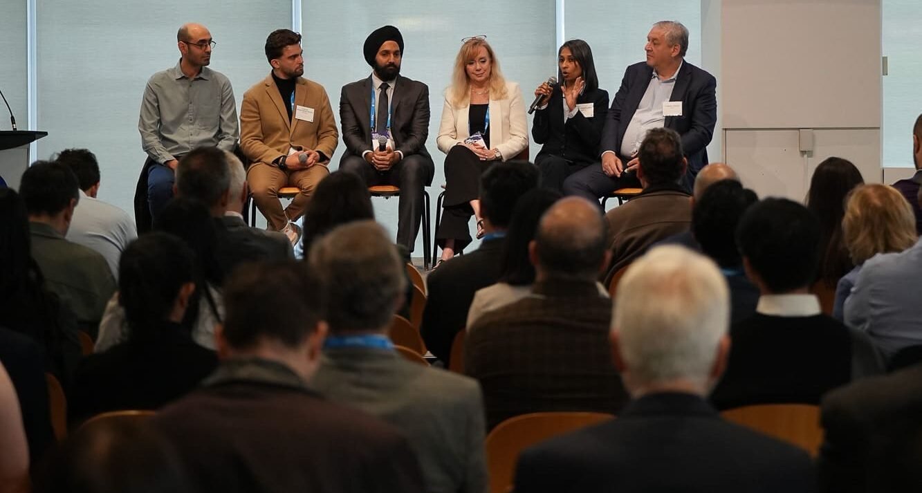 A wide shot of a panel discussion titled "Advancing global mobility through collaboration" taking place at the MaRS Toyota Mobility Forum. Seven panelists are seated on stage, facing a large, engaged audience. A screen above them displays their names and titles, including Tracey McGillivray of Axtion Independence Mobility, Pooja Viswanathan of Braze Mobility, and Manmeet Maggu of Trexo Robotics. The moderator, David Hengeveld, is seated on the far right.