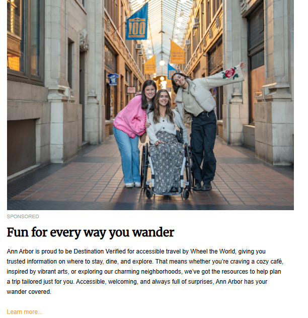 A full-length photo of three young women posing and smiling together inside a covered, arched pedestrian walkway or arcade lined with brick and windows. The woman in the center is seated in a manual wheelchair, wearing a light-colored cardigan and a long patterned skirt. The two women flanking her stand close, with one in a pink sweater and the other in a cream jacket, both with their arms outstretched in excitement. The image promotes the article "Fun for every way you wander" about accessible travel in Ann Arbor.