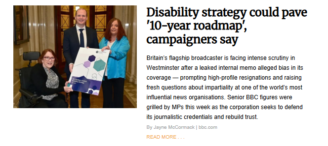 A screenshot of the article titled, "Disability strategy could pave '10-year roadmap,' campaigners say". The image shows three people—a man in a suit and two women, one of whom is seated in a wheelchair—standing indoors and holding a large paper titled, "Disability Strategy."